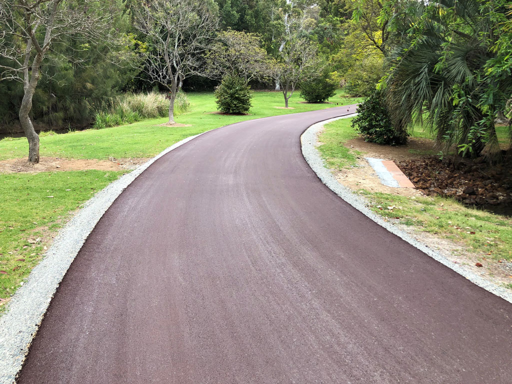 A recycled asphalt driveway installed by NK Asphalt leading off around the corner in a leafy suburb.